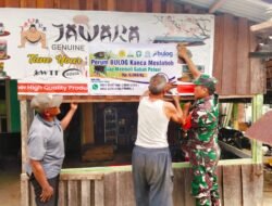 Ringankan Beban Warga, Babinsa Bantu Pasang Spanduk Ketahanan Pangan di Kantor Desa